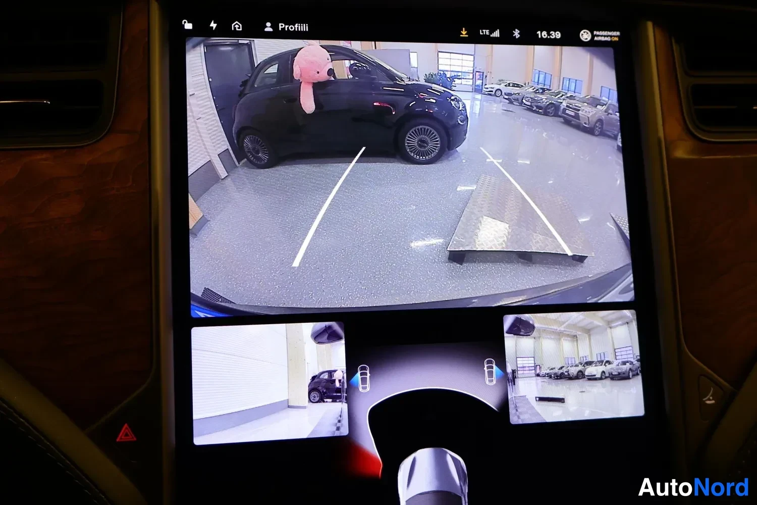 Muu: Kosketusnäytön kamera- ja pysäköintinäkymä autotallissa, jossa tumma pieni auto ja useita muita autoja taustalla.