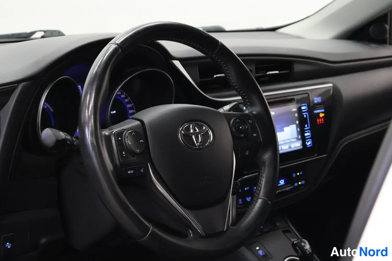 Edestä: Toyota-merkillä varustettu ohjauspyörä, kojelaudan mittarit ja kosketusnäytöllinen infotainment-järjestelmä.