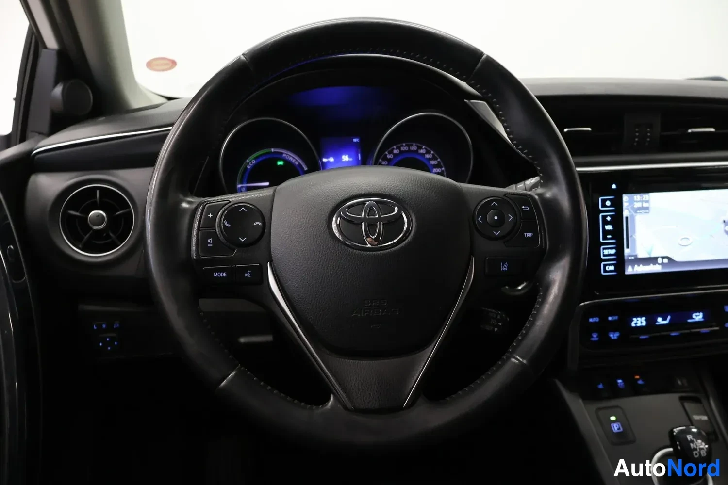 Edestä: Ohjauspyörä Toyota-emblemillä, hybridin mittaristo ja navigointinäytöllinen keskusyksikkö.