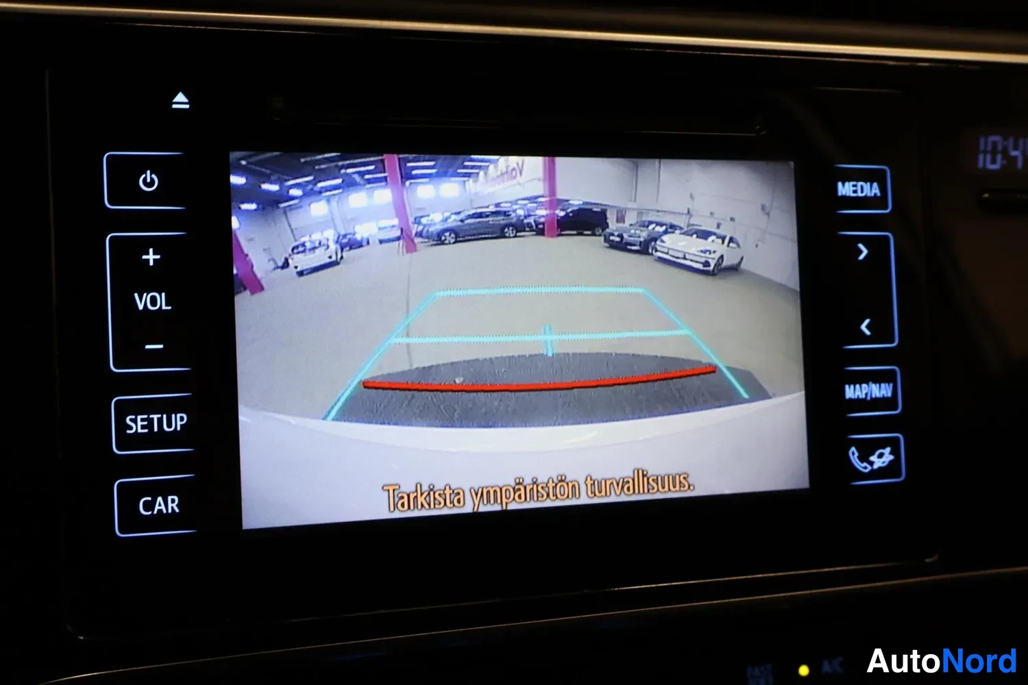 Muu: Infotainment-näyttö, jossa taustakameran kuva parkkihallista ja teksti 'Tarkista ympäristön turvallisuus.'