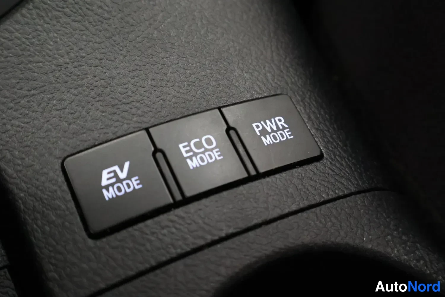 Yksityiskohta: Close-up of three black push buttons with white text on dark plastic interior trim. Left button reads EV MODE, middle reads ECO MODE, right reads PWR MODE.