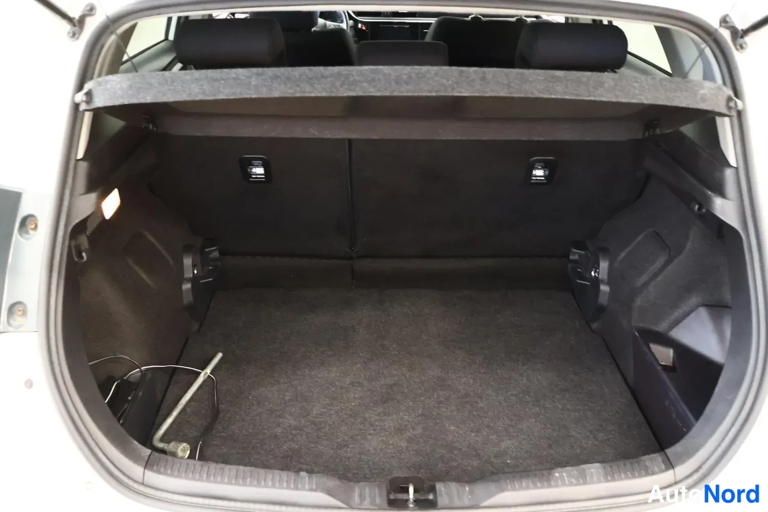 Takaviisto: Open boot of a car from rear angle showing carpeted floor, retractable cargo cover extended, and four rear seat headrests visible above.