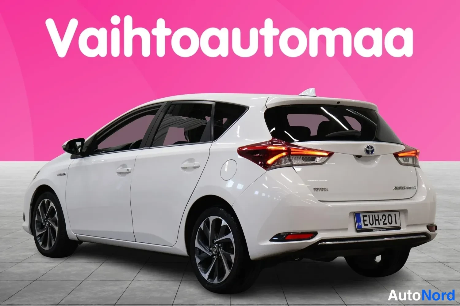 Takaviisto: Valkoisen hatchbackin takakulma vasemmalta, punaiset takavalot, Toyota-merkki ja -rekisterikilpi, vaaleansininen tausta.