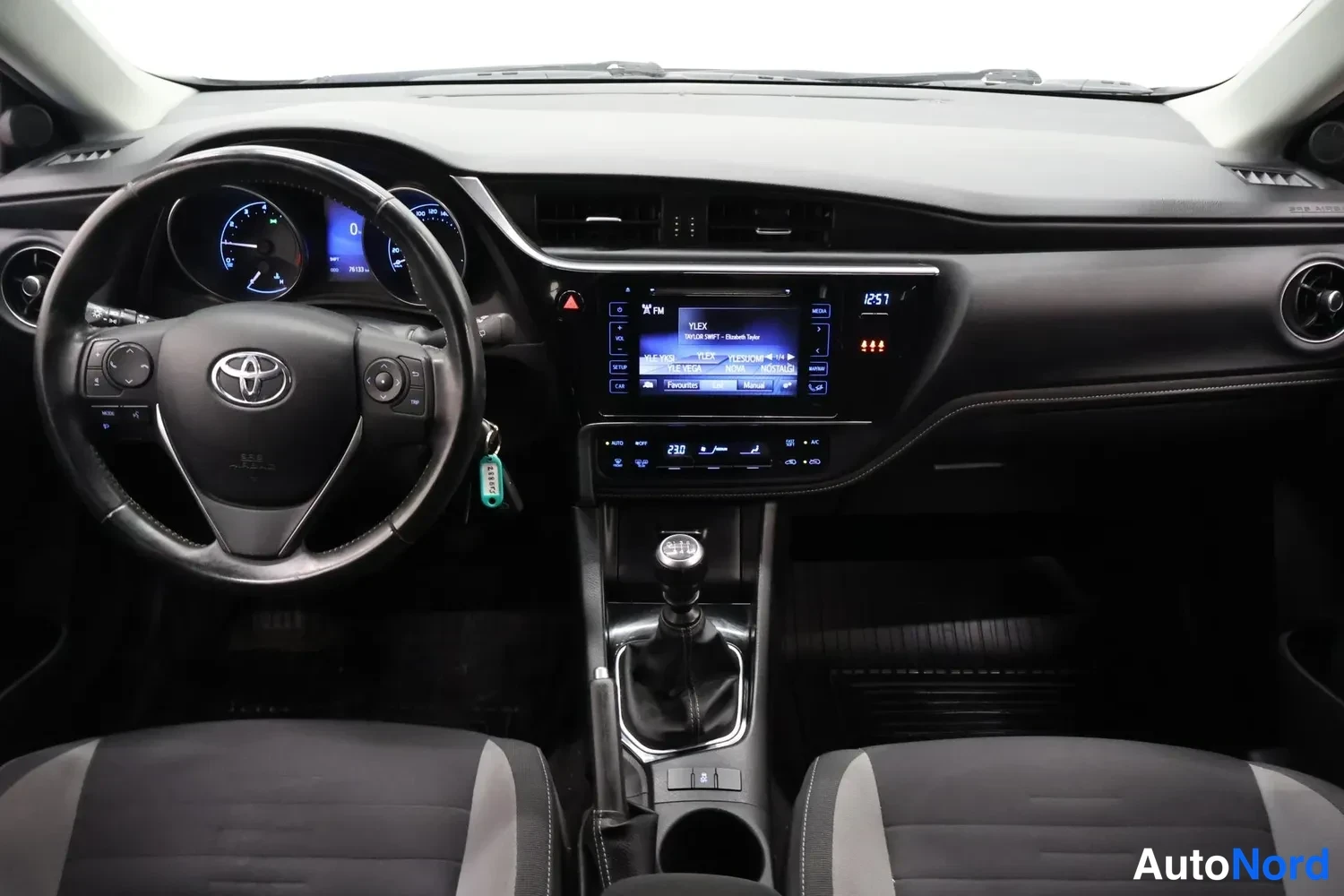 Muu: Koko kojelauta etusivulta: Toyota-ohjauspyörä, mittaristo, kosketusnäytöllinen radiopaneeli (YLEX, 12:57), manuaalivaihtokeppä ja kankaat etupenkit.