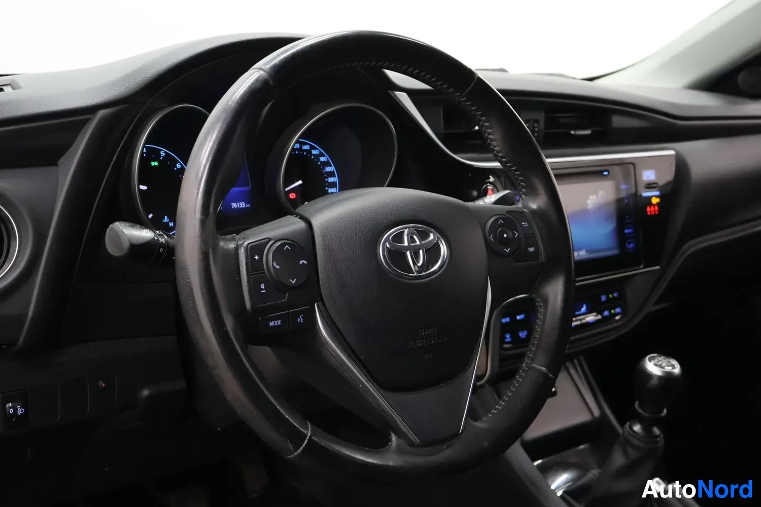 Muu: Kuljettajan näkökulma ohjaamosta: Toyota-merkkiohjauspyörä, mittaristo ja kosketusnäytöllinen radio, manuaalivaihtokeppä oikealla.