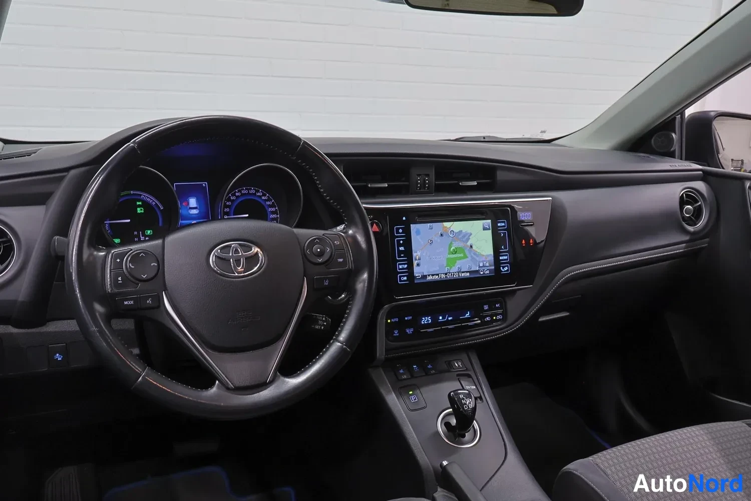 Etuviisto, nokka vasemmalle: Ohjaamo Toyota Auriksesta: ohjauspyörä, hybridi mittaristo, kosketusnäytöllinen navigointijärjestelmä ja automaattivaihteen valitsin.