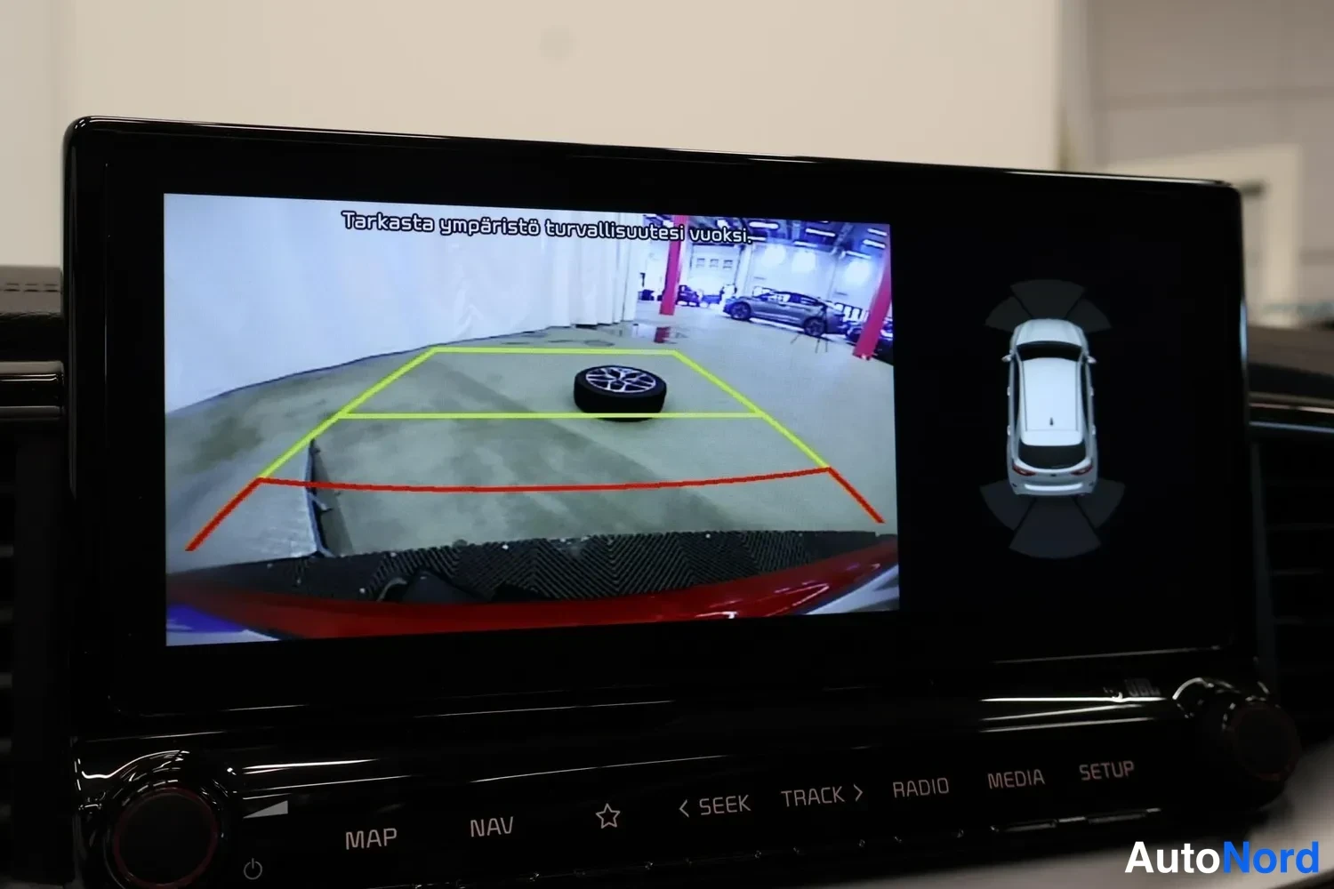 Muu: Infotainment-näytöllä näkyy peruutuskameran kuva opastuskäyrillä ja tekstillä 'Tarkasta ympäristö turvallisuutesi vuoksi'.