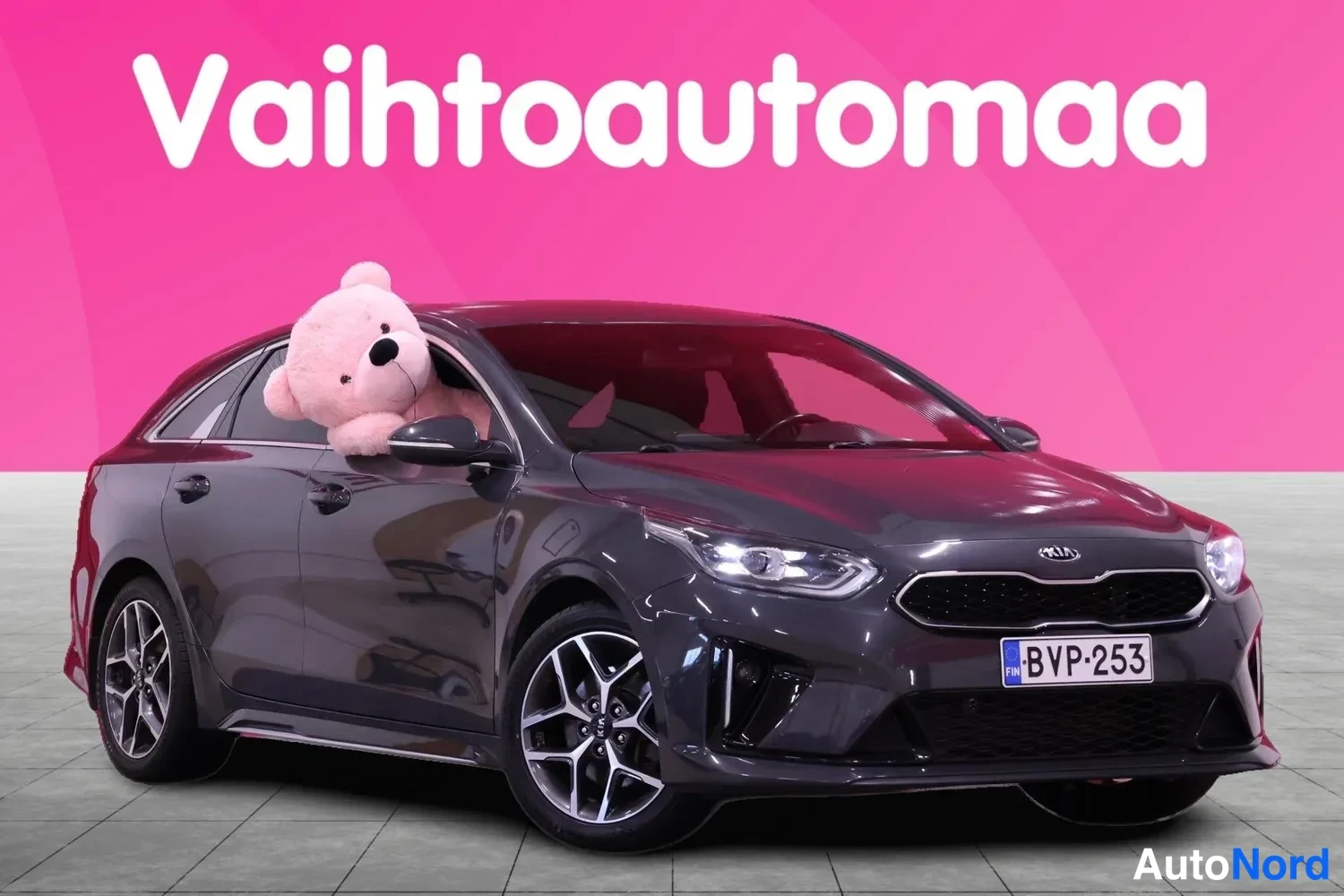 Etuviisto, nokka oikealle: Kia ProCeed -farmarikin auto, tummanharmaa, etuviisto kuva; pehmolelu takavasemman ikkunan vieressä, rekisteri.