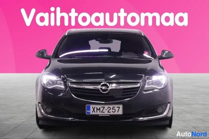 Edestä: Mustan auton suora etunäkymä, etugrilli ja Merkki-logo, rekisterikilpi, pinkki tausta.