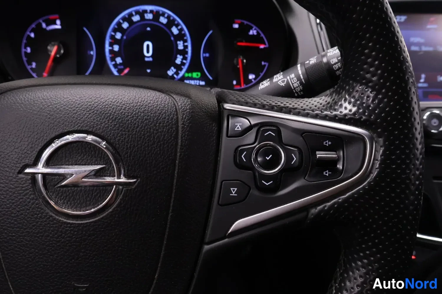 Muu: Ohjauspyörän keskusosa Opel-logolla ja monitoiminapeilla, taustalla mittariston näyttö.