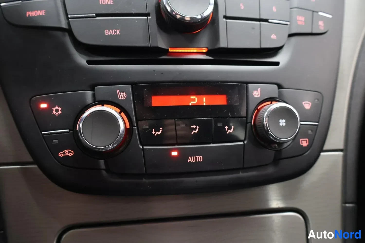 Yksityiskohta: Kohtakuva auton kojelautaan sisältyvästä ilmastointipaneelista, jossa näkyy AUTO-merkintä, lämpötilanäyttö ja lämmitettävien istuimien painikkeet.
