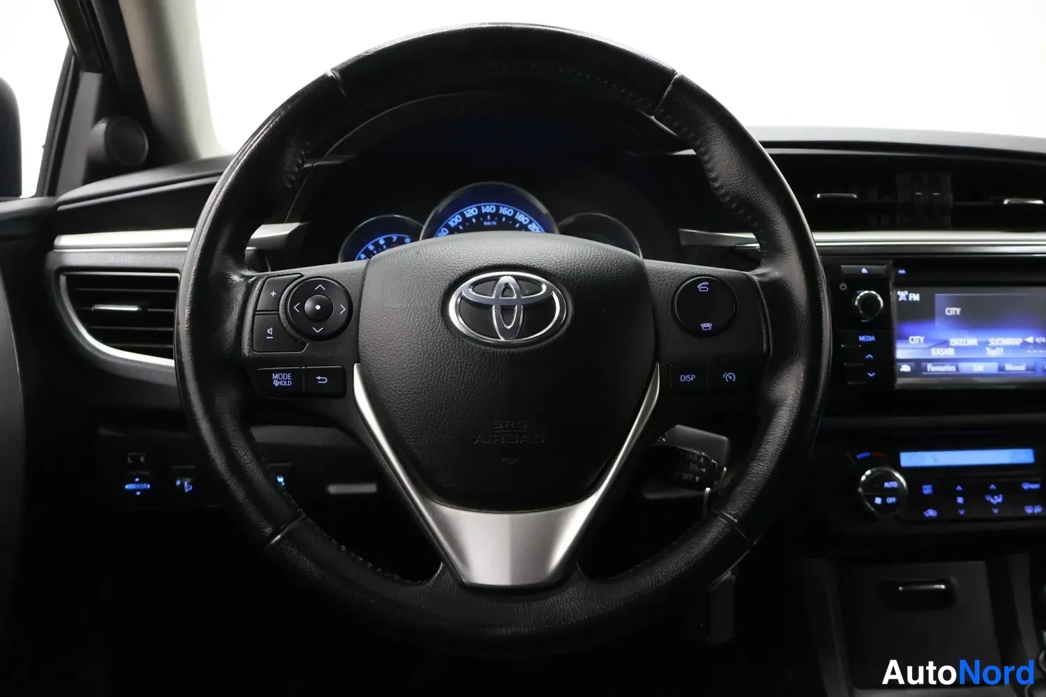 Muu: Ohjauspyörä ja kojelaudan näkymä, Toyota-merkki pyörän keskiössä ja mittaristo taustalla.