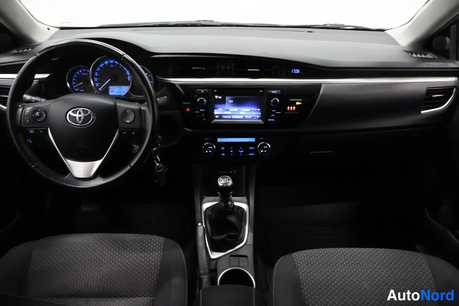 Yksityiskohta: Toyota Corolla 2014 - sisätilat: ohjaamo ja kojelauta etusijoilta kuvattuna, musta sisusta, manuaalivaihteisto ja kosketusnäytöllä varustettu radiolaite.