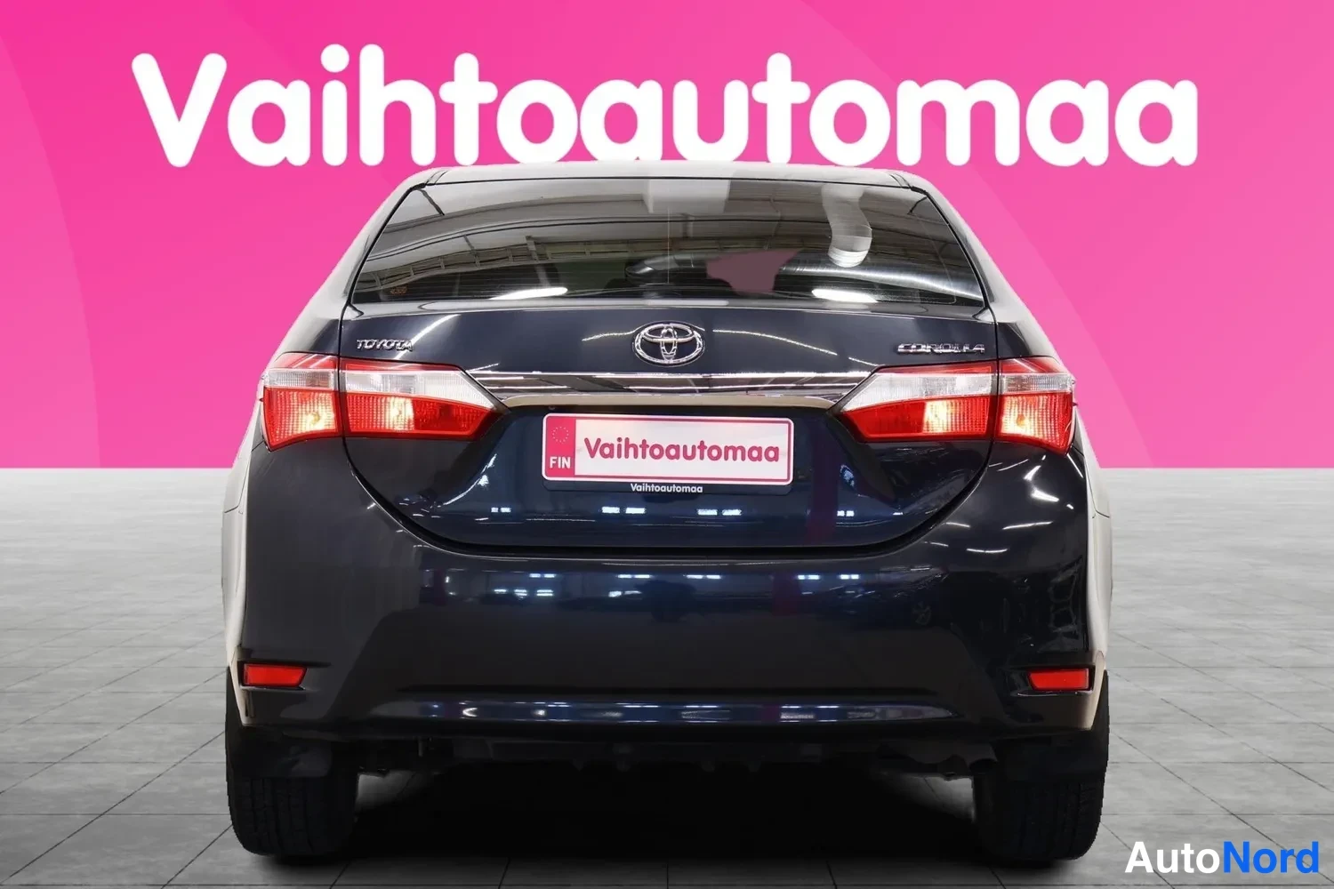 Takaa: Tummanharmaan Toyota Corolla -sedanin takaosa suoraan takaa; punaiset takavalot, Toyota-merkki ja Corolla-teksti näkyvät rekisterikilven paikkaa peittävän Vahto