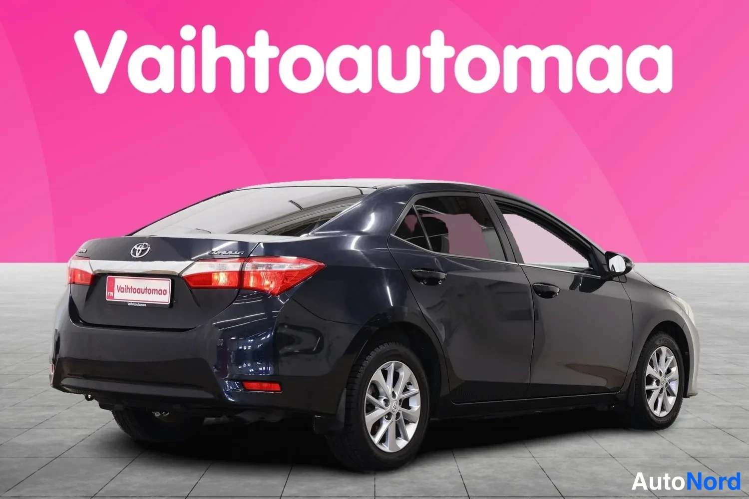 Takaviisto: Tummanharmaa Toyota Corolla -sedan takaviistosta vasemmalta; neljä ovea, takavalot ja hopeat kevytmetallivanteet näkyvät vaaleanpunaisella taustalla.