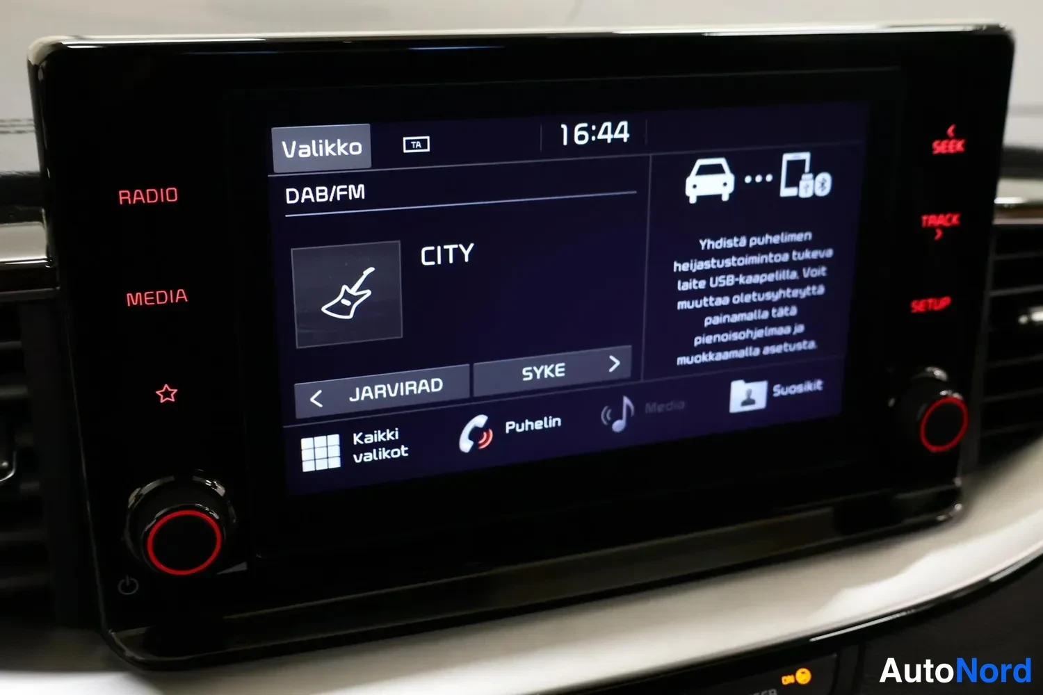 Muu: Infotainment-näyttö: DAB/FM-radio valikossa, asema CITY, kellonaika 16:44 ja puhelimen yhdistämisohje.