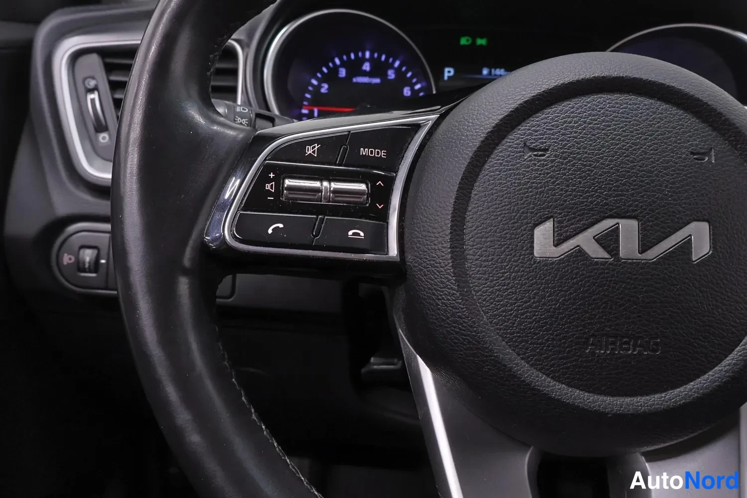 Muu: Lähikuva ohjauspyörästä: KIA-logo, AIRBAG-teksti, äänentoiston ja puhelun nappiohjaimet sekä MODE-painike; takaosassa kojelaudan mittarit.