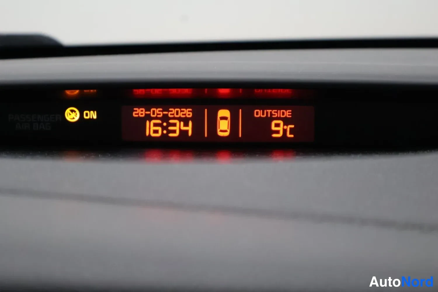 Yksityiskohta: Kojelaudan näyttö, jossa kellonaika 16:34, päivämäärä 28-05-2026, ulkolämpötila 9 °C ja matkustajan turvatyynyn ON-merkkivalo.