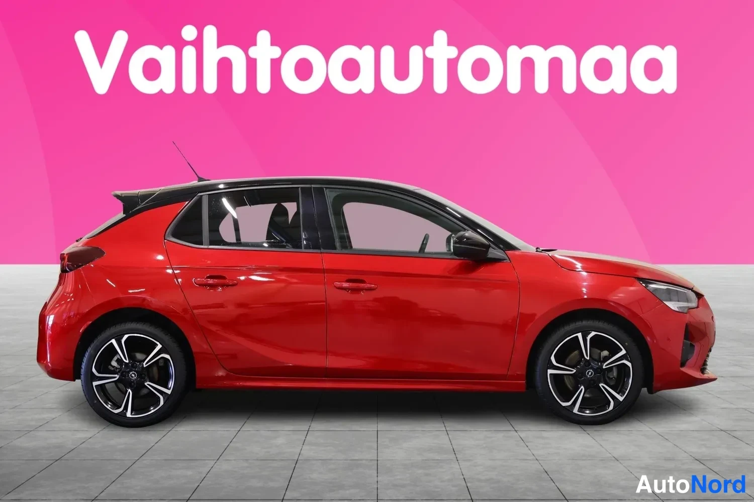 Etuviisto, nokka oikealle: Punainen viistoperäinen henkilöauto sivusta oikeasta suunnasta, musta kattolineisto, vaaleanharmaa lattia ja pinkki tausta.