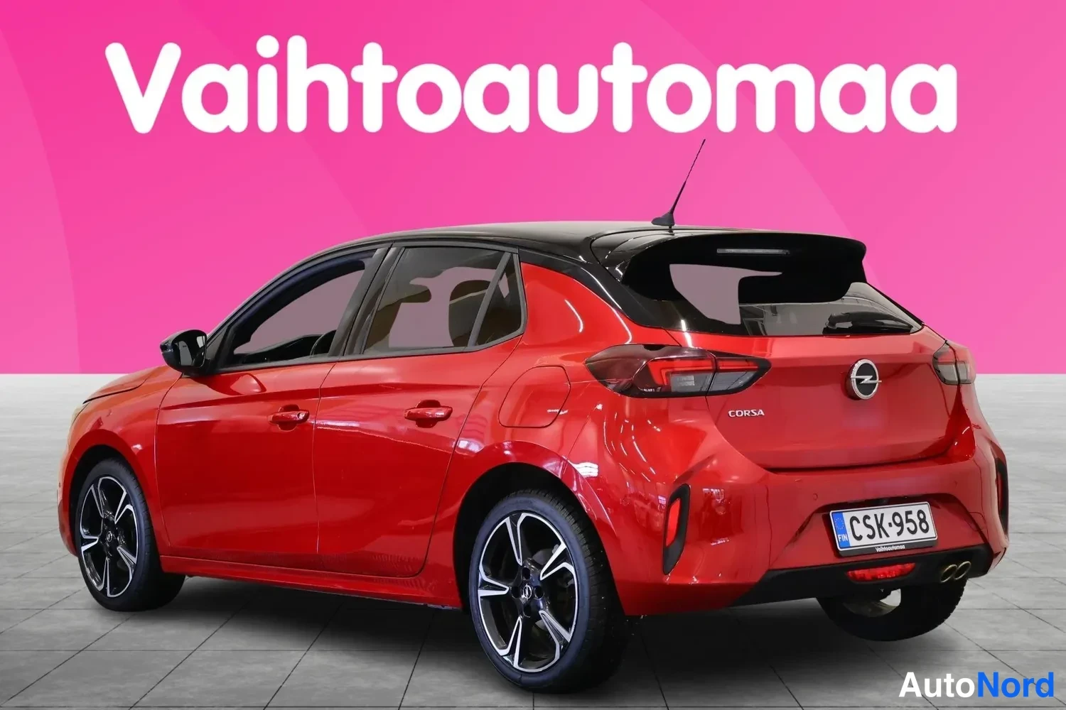 Takaviisto: Punainen Opel Corsa -viistoperä takaviistosta oikealta kuvattuna, musta katto ja kaksiosainen takavalaisin näkyvät, rekisteritunnus.