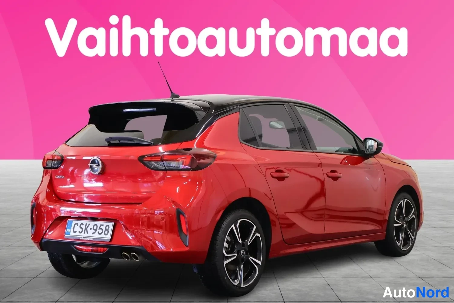 Takaviisto: Punainen Opel Corsa -viistoperä takaviistosta vasemmalta kuvattuna, musta katto, viitospyörät ja rekisteritunnus näkyvät.