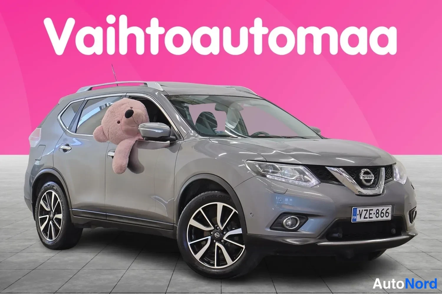 Etuviisto, nokka oikealle: Harmaa Nissan X-Trail etu­kolmasosa­vasemmaltta kuvattuna myyntihallissa, maski ja etupyörä näkyvät, rekisteritunnus.