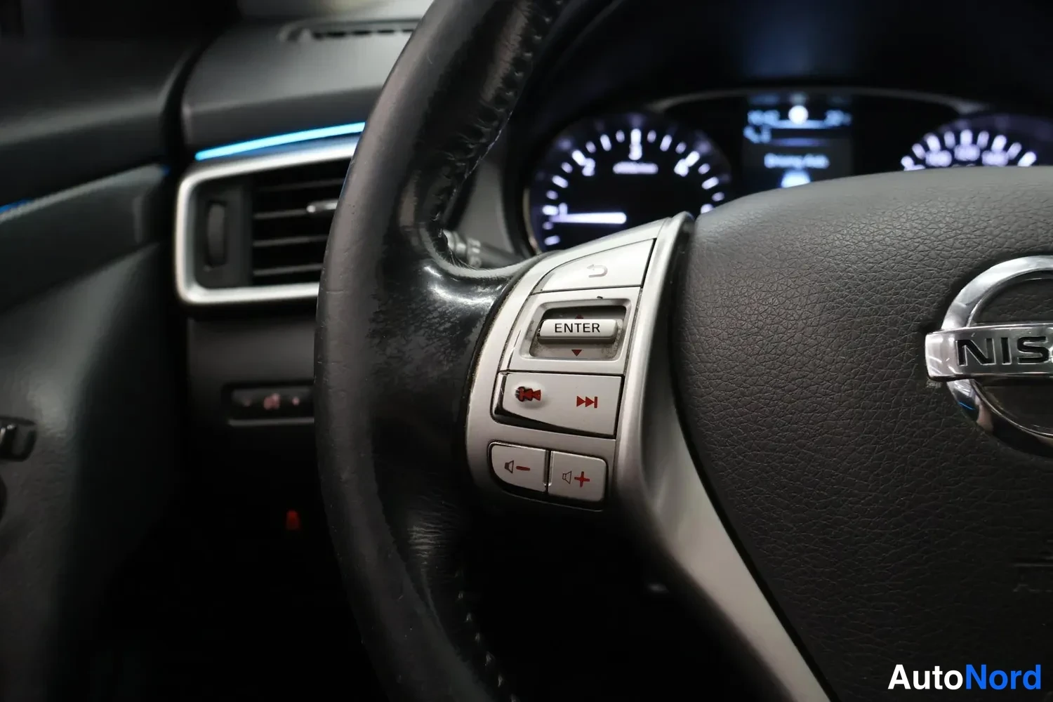 Muu: Rattipöydän vasemman palkin painikkeet lähikuvassa ENTER- ja äänentoisto-ohjaimilla, Nissan-logo osittain näkyvissä.