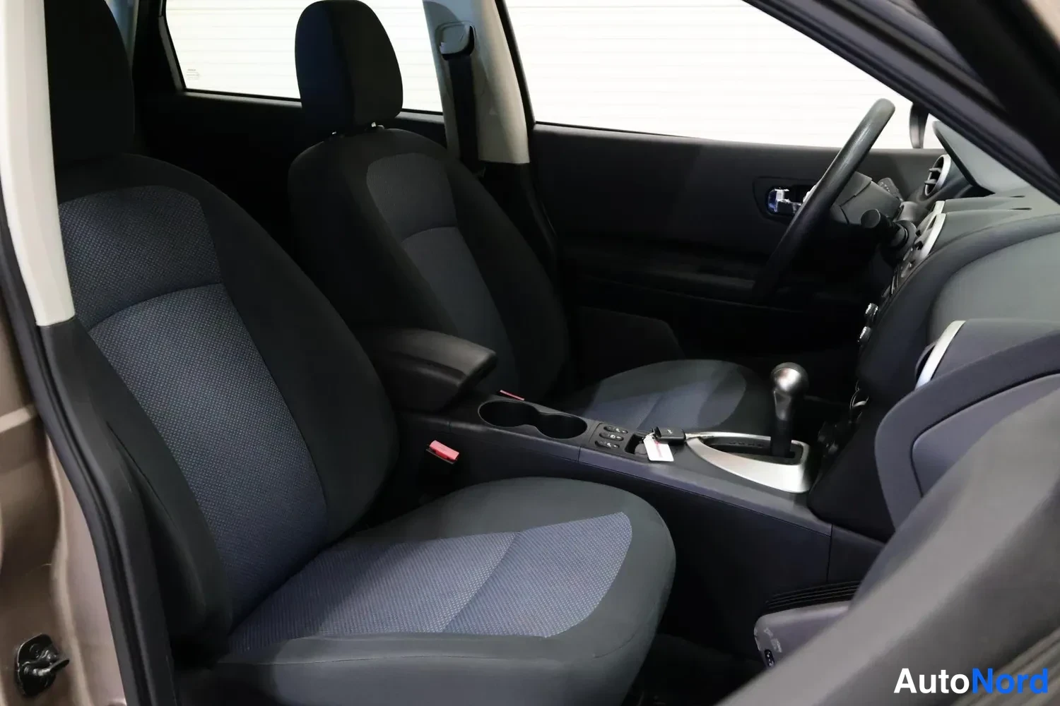 Muu: Nissan Qashqain etuistuimet ja kojelauta sisältä; tummansiniset kangasistuimet, automaattivaihteiston valitsin näkyvissä.