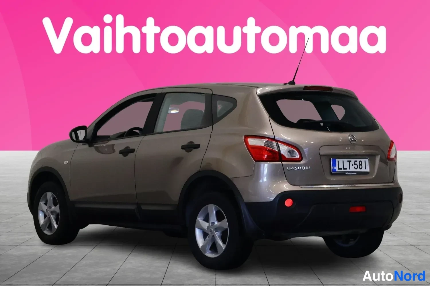 Takaviisto: Beige Nissan Qashqai -maastauto vinosti takaa oikealta kuvattuna, Qashqai-merkintä ja rekisterikilpi näkyvissä.