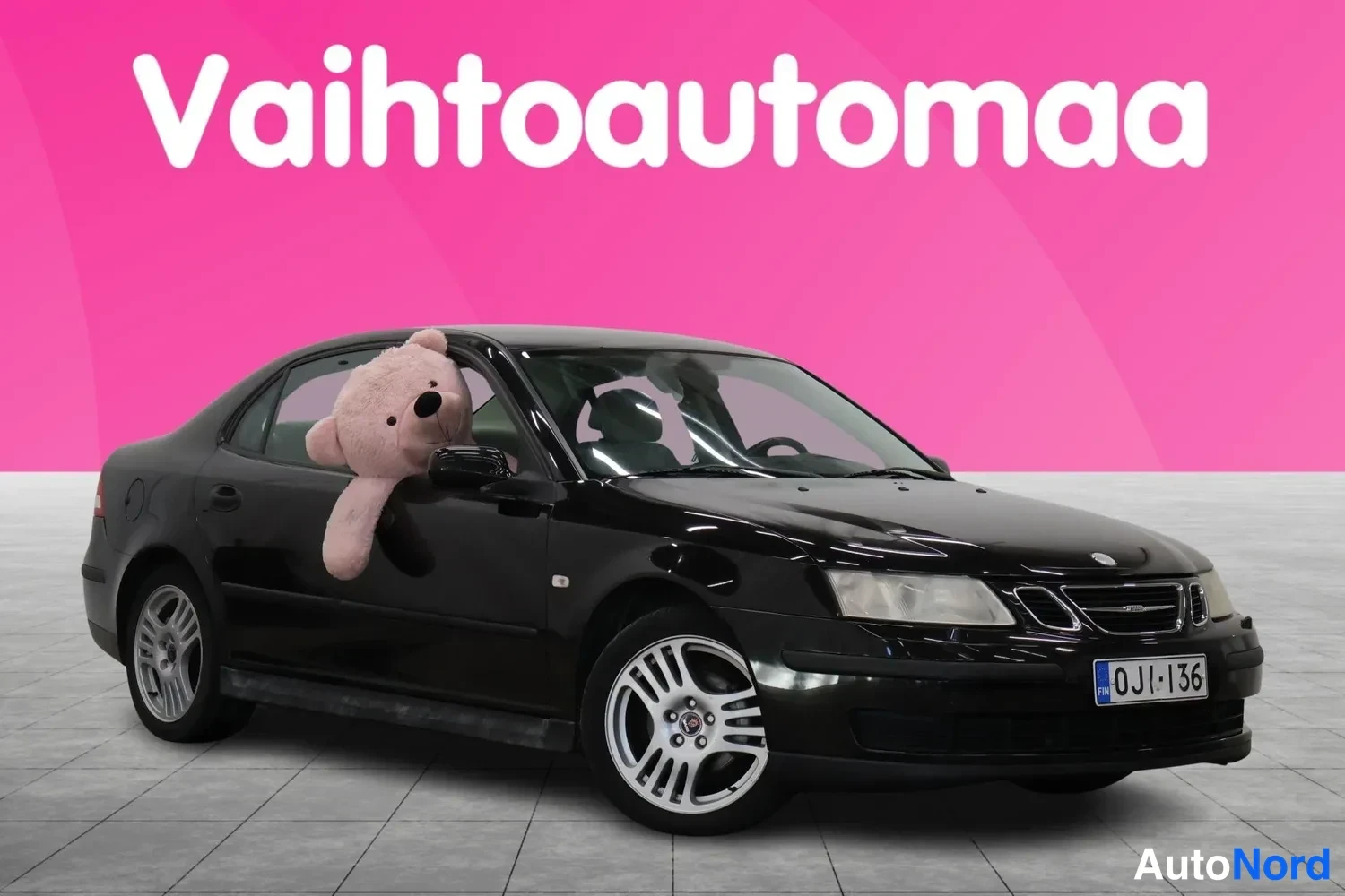 Etuviisto, nokka oikealle: Mustan Saab 9-3 -sedanin etuosa ja oikea sivu kolmasosakulmassa, pehmolelu takapyyhkeä ikkunasta