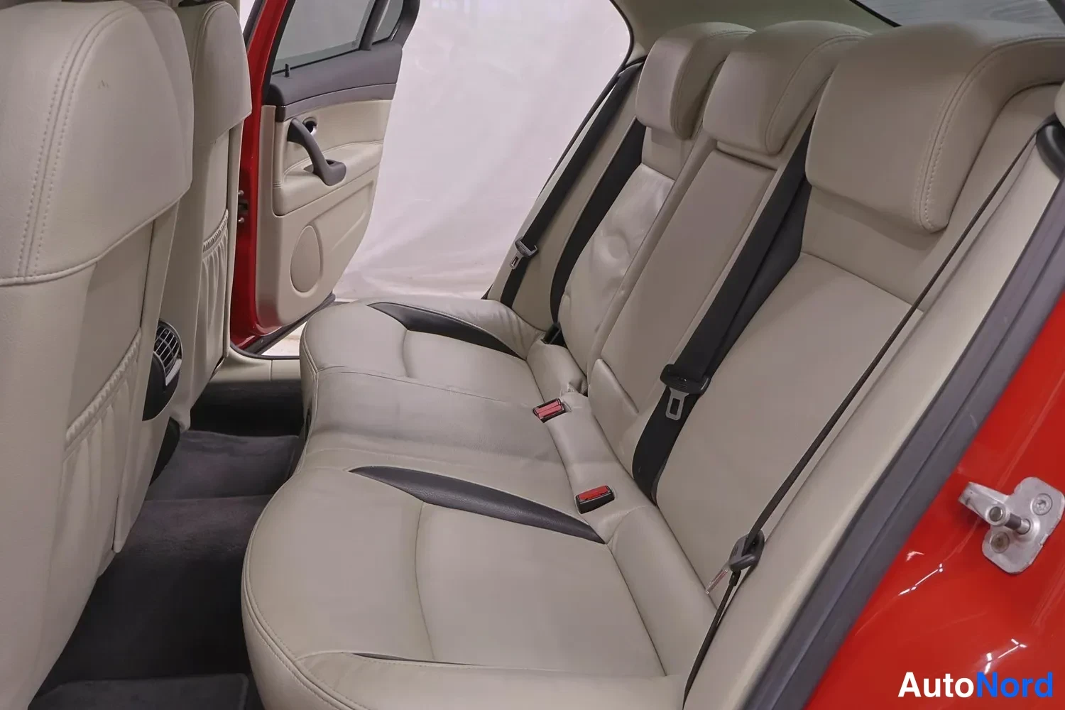 Muu: Takapenkin sisätila: vaalea nahkainen sohvatyylinen takapenkkiosasto ja avattu takaovi punaisella ovipaneelilla.