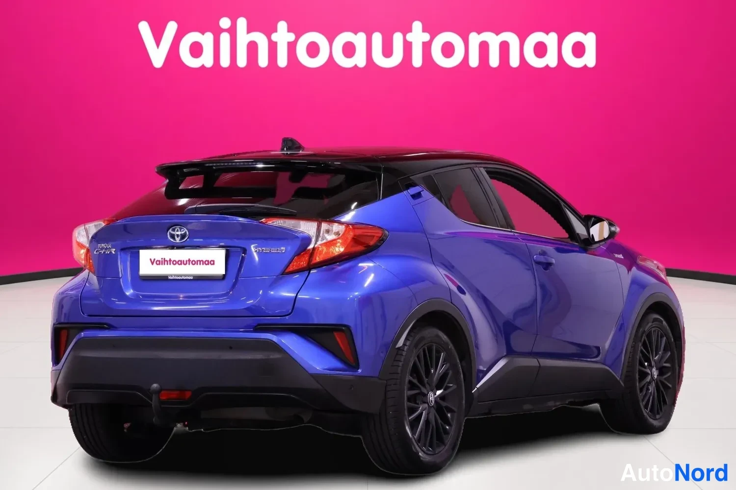 Takaviisto: Sininen Toyota C-HR takaa kolmannenvesan kulmasta, tumma katto ja mustat vanteet, Vahtoautomaan taustapenkki