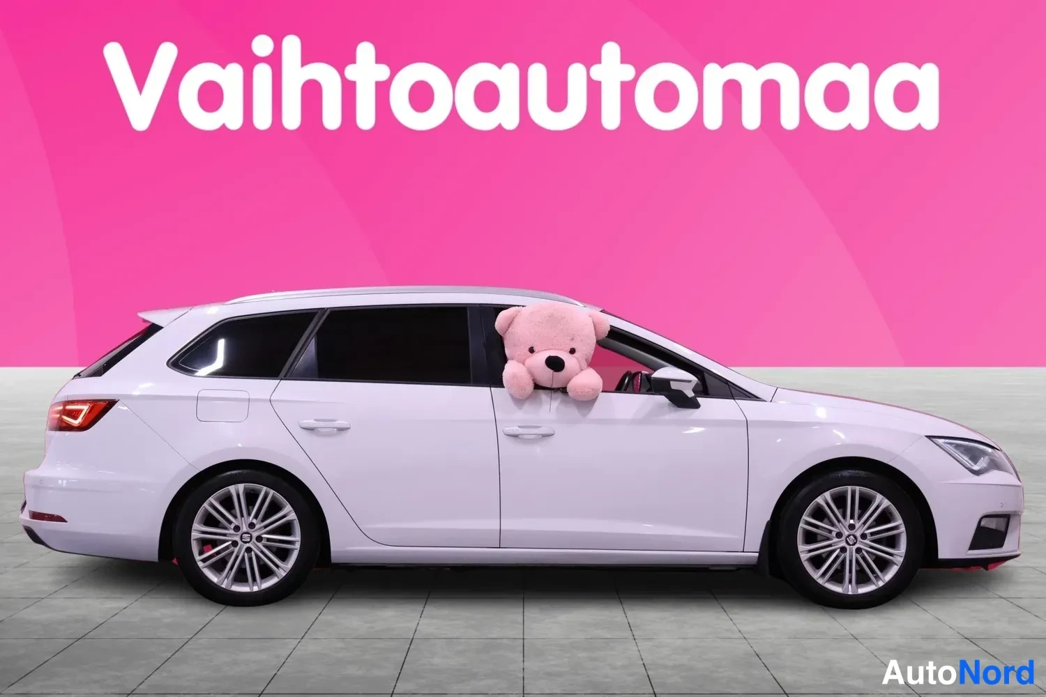 Sivulta: Valkoinen farmariauto sivulta, pinkki tausta ja Vaihtoautomaat-logo ylhäällä