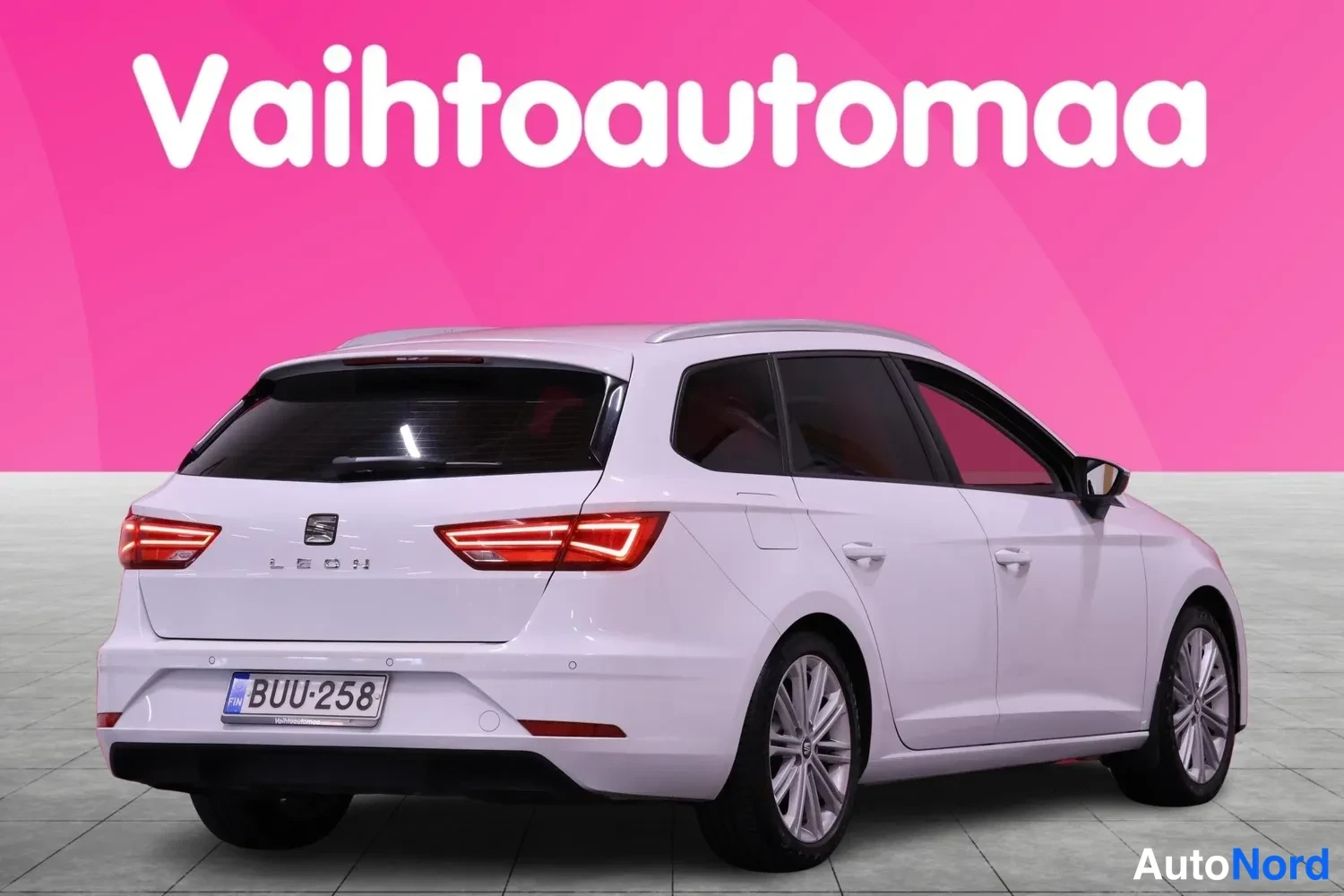 Takaviisto: Valkoinen farmariauto takaa kolmivartalokulmassa, pinkki tausta ja Vaihtoautomaat-logo ylhäällä