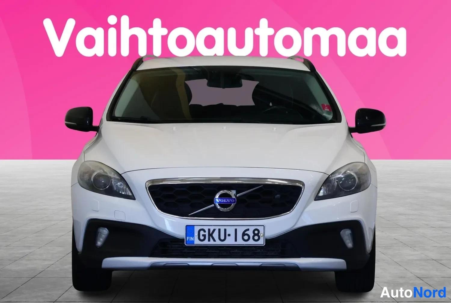 Edestä: Valkoinen henkilöauto suoraan edestä, etusäleikkö ja Volvo-merkki, rekisterikilpi.