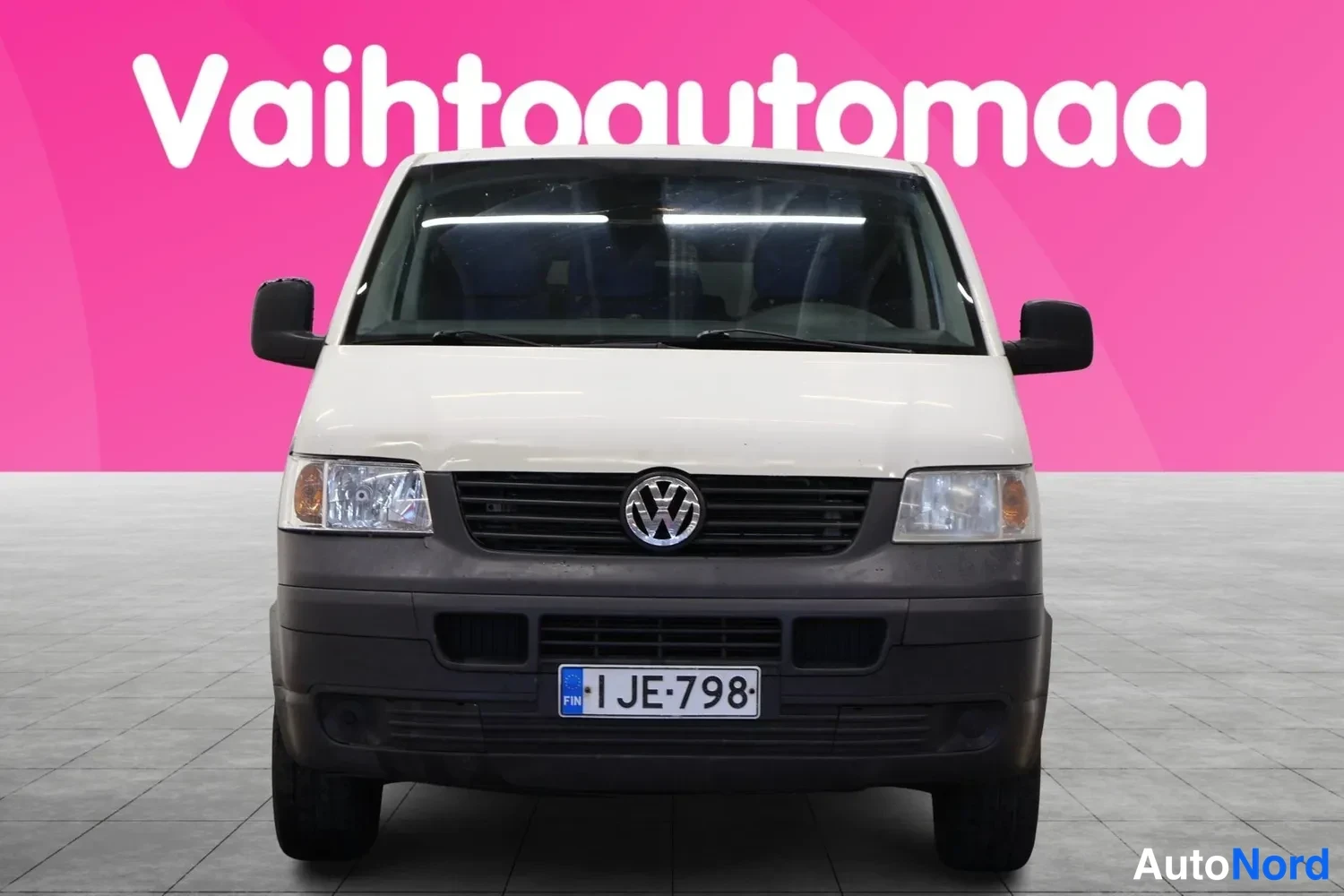Edestä: Valkoinen pakettiauto suoraan edestäpäin, VW-merkki ja rekisterikilpi JE-798 näkyvissä.