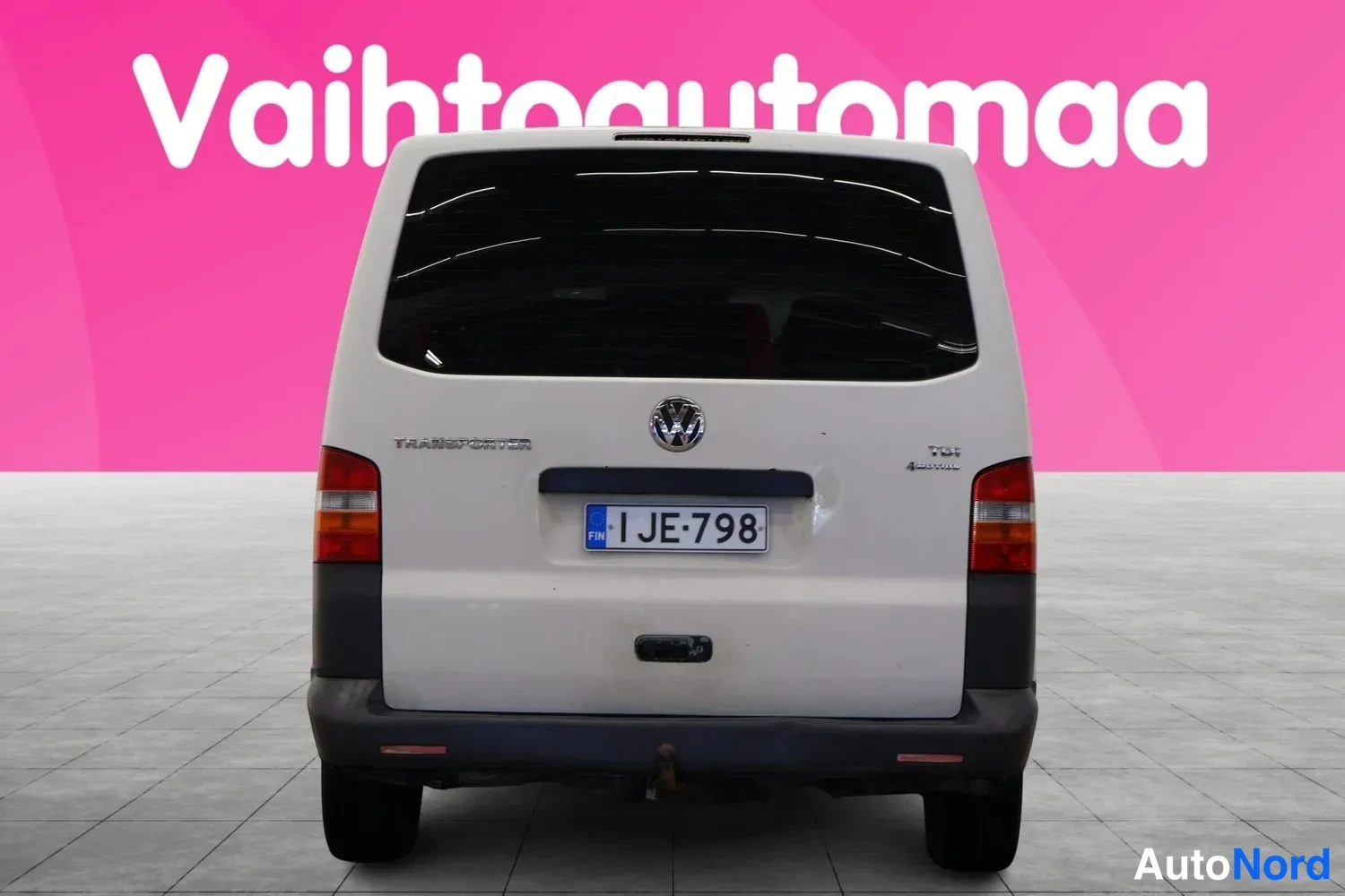 Takaa: Valkoisen pakettiauton takanäkymä: rekisterikilpi 1 JE-798, TRANSPORTER- ja TDI 4MOTION-tekstit, korkea pysähtymisvalo.
