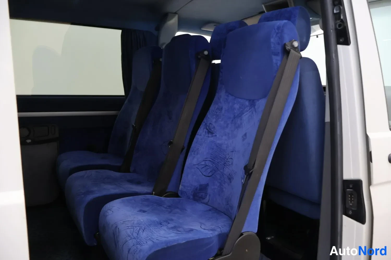 Muu: Auton sisätilat avoimesta ovesta katsottuna: kolme sinistä istuinta kolmipiste-hihnoin.