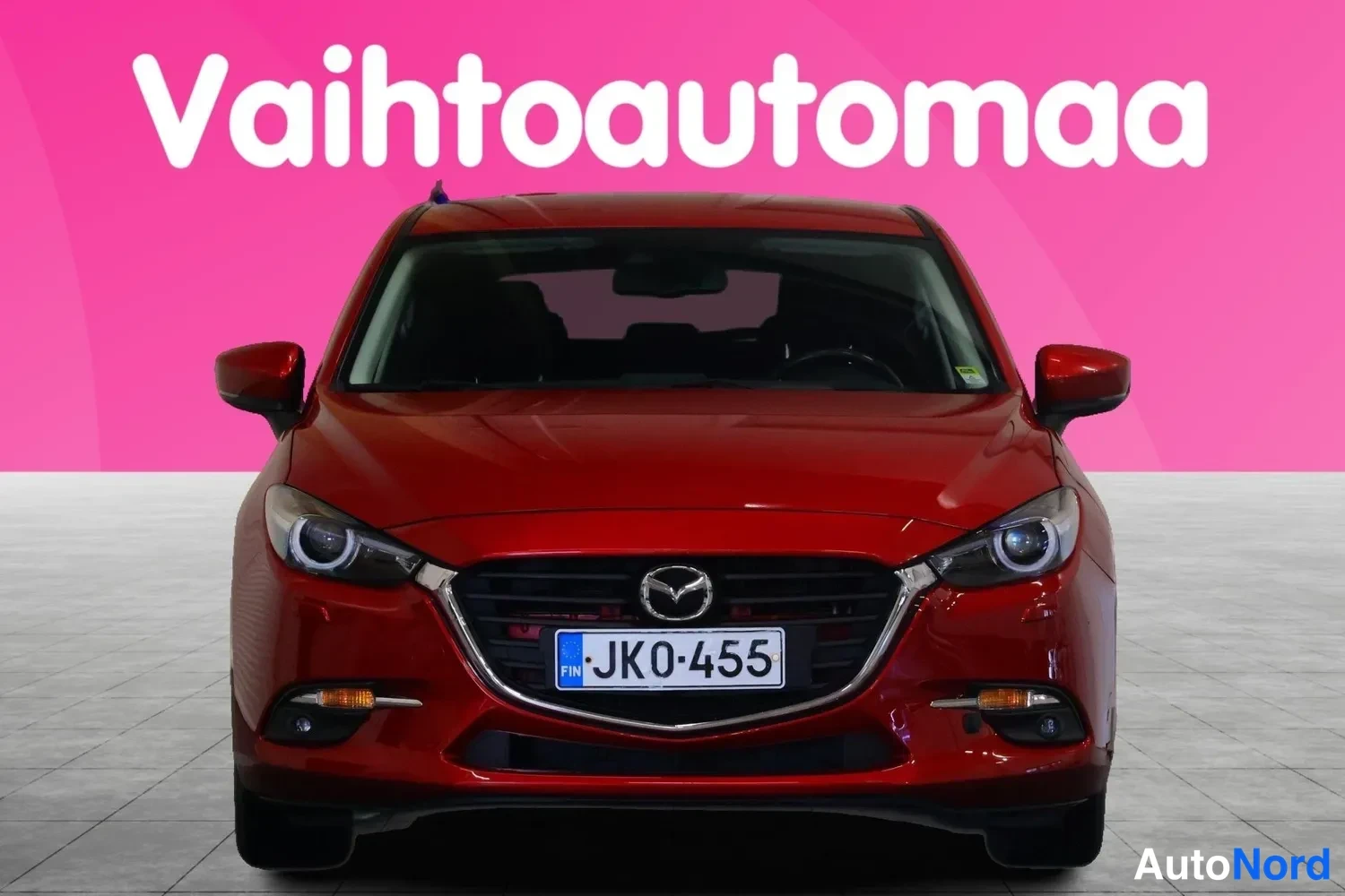 Edestä: Punainen Mazda 3 -henkilöauto suoraan edestä kuvattuna, rekisterikilpi JK0-455.