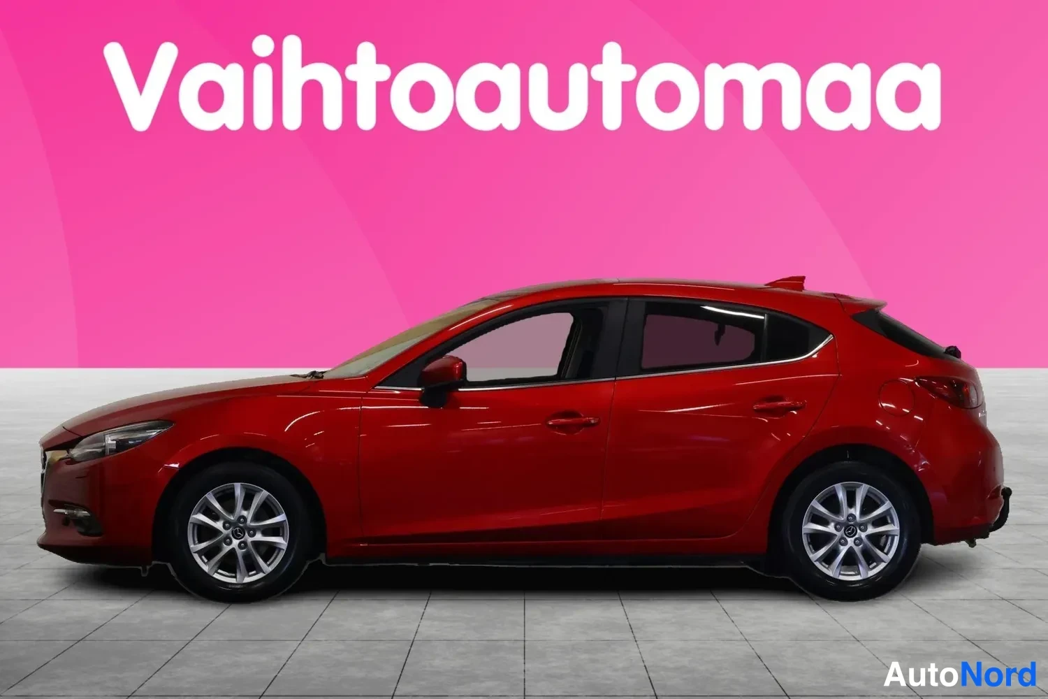 Etuviisto, nokka vasemmalle: Punaisen Mazda3-hatchbackin etukulmanäyttö vasemmalta eteen, studioasennus pinkillä taustalla.