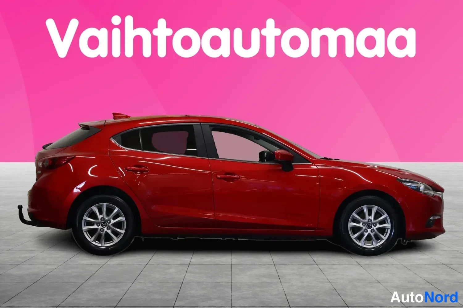 Etuviisto, nokka oikealle: Punainen Mazda 3 -farmari sivulta oikeaan etukulmaan kuvattuna, vaalea studiotaustainen myyntikuva.