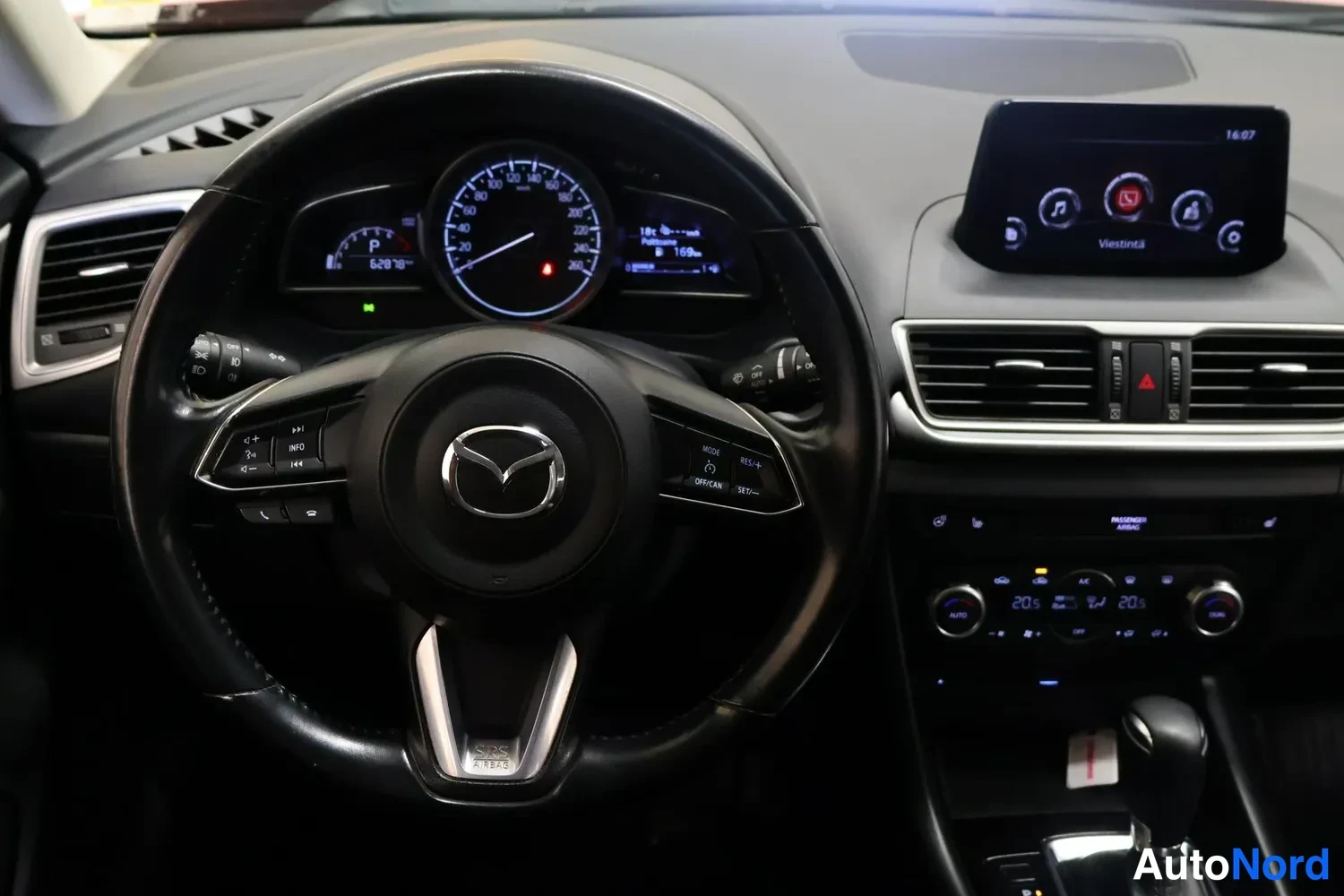 Yksityiskohta: Ohjaamo etupuolelta: Mazda-ohjauspyörä, mittaristo ja kosketusnäyttö, automaattivaihteiston valitsin.