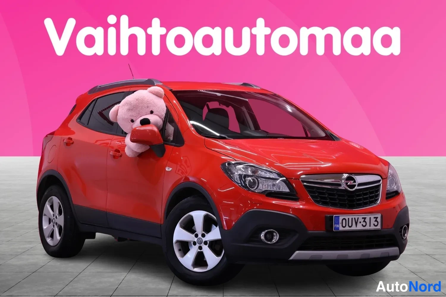 Etuviisto, nokka oikealle: Punainen Opel Mokka esitellään etukolmasosakulmasta, nokka oikealla; peilistä kurkistaa pehmolelu.