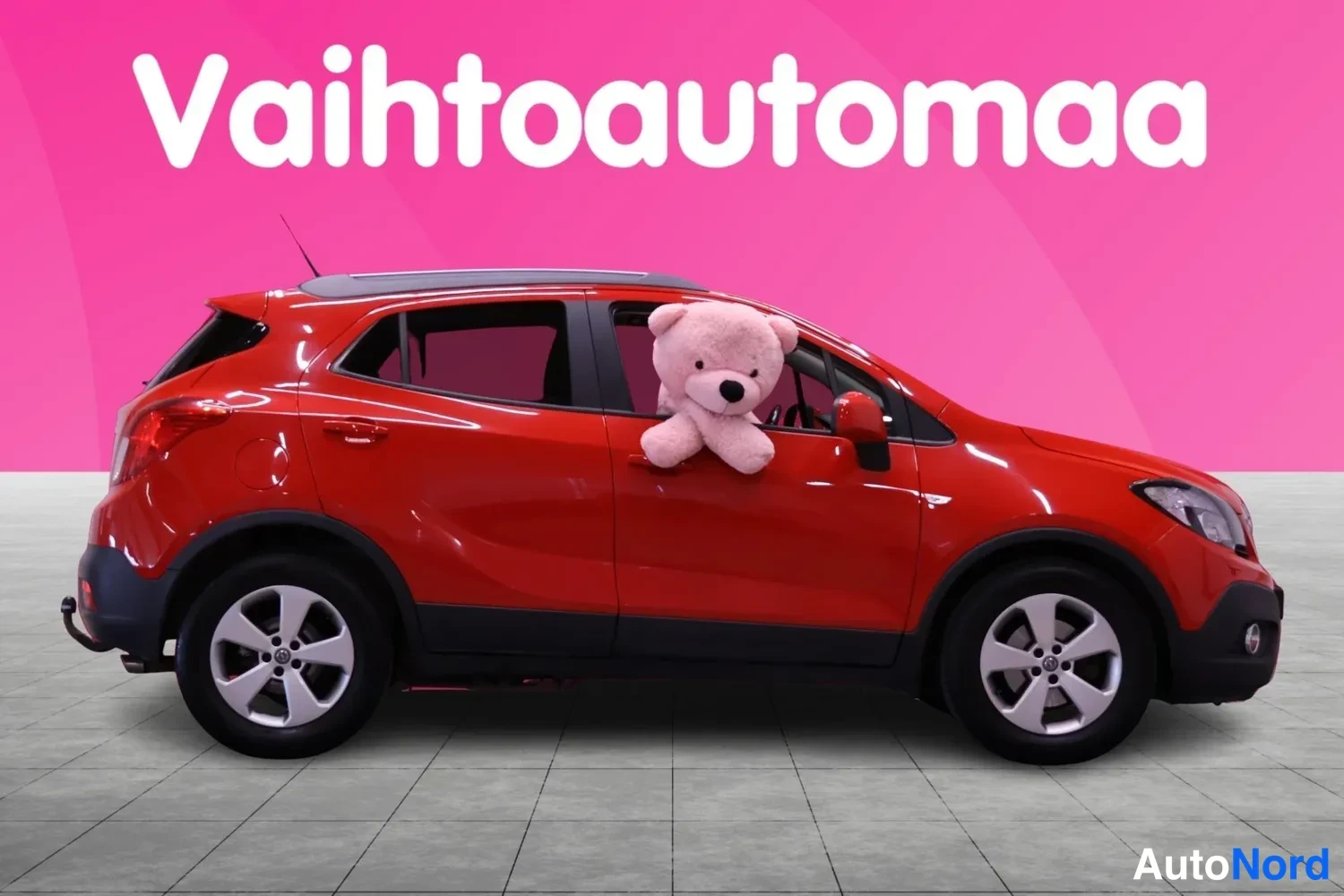 Sivulta: Punainen Opel Mokka sivusta vasen kylki näkyvissä, ikkunasta kurkistaa pehmolelu.