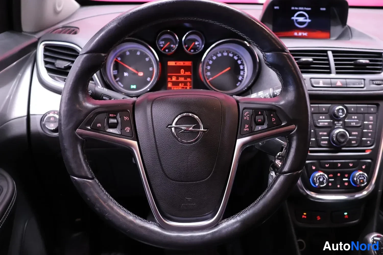 Muu: Ohjauspyörä lähikuvassa Opel-logolla, mittarit ja ohjauspyörän painikkeet näkyvissä, keskikonsoli ja ilmastointisäätimet oikealla.
