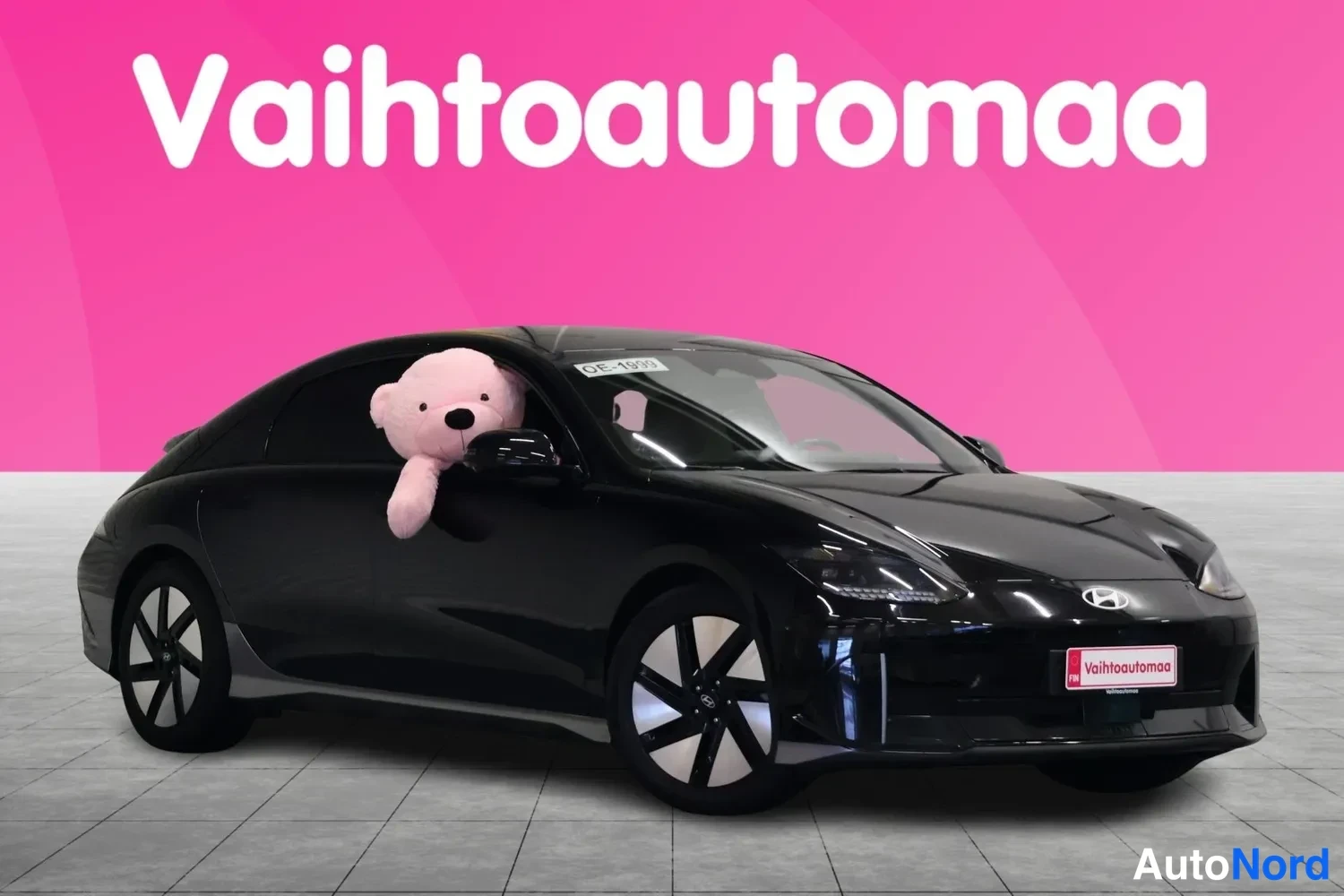 Etuviisto, nokka oikealle: Musta Hyundai Ioniq 6 etuosa oikealta kolmannelta, pehmolelu ikkunassa.