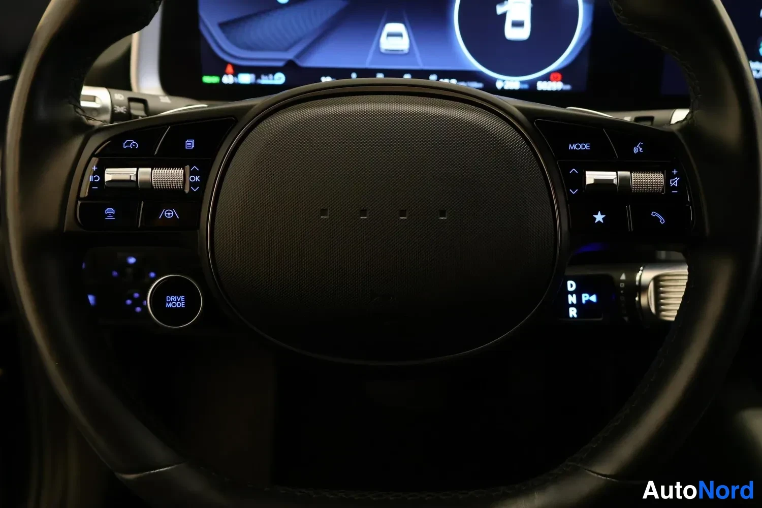 Muu: Ohjauspyörän ja kojelaudan näytön lähikuva; pyörästä näkyvät MODE-, OK- ja DRIVE MODE -painikkeet sekä vaihteenvalinnan P/D/N/R-merkinnät.