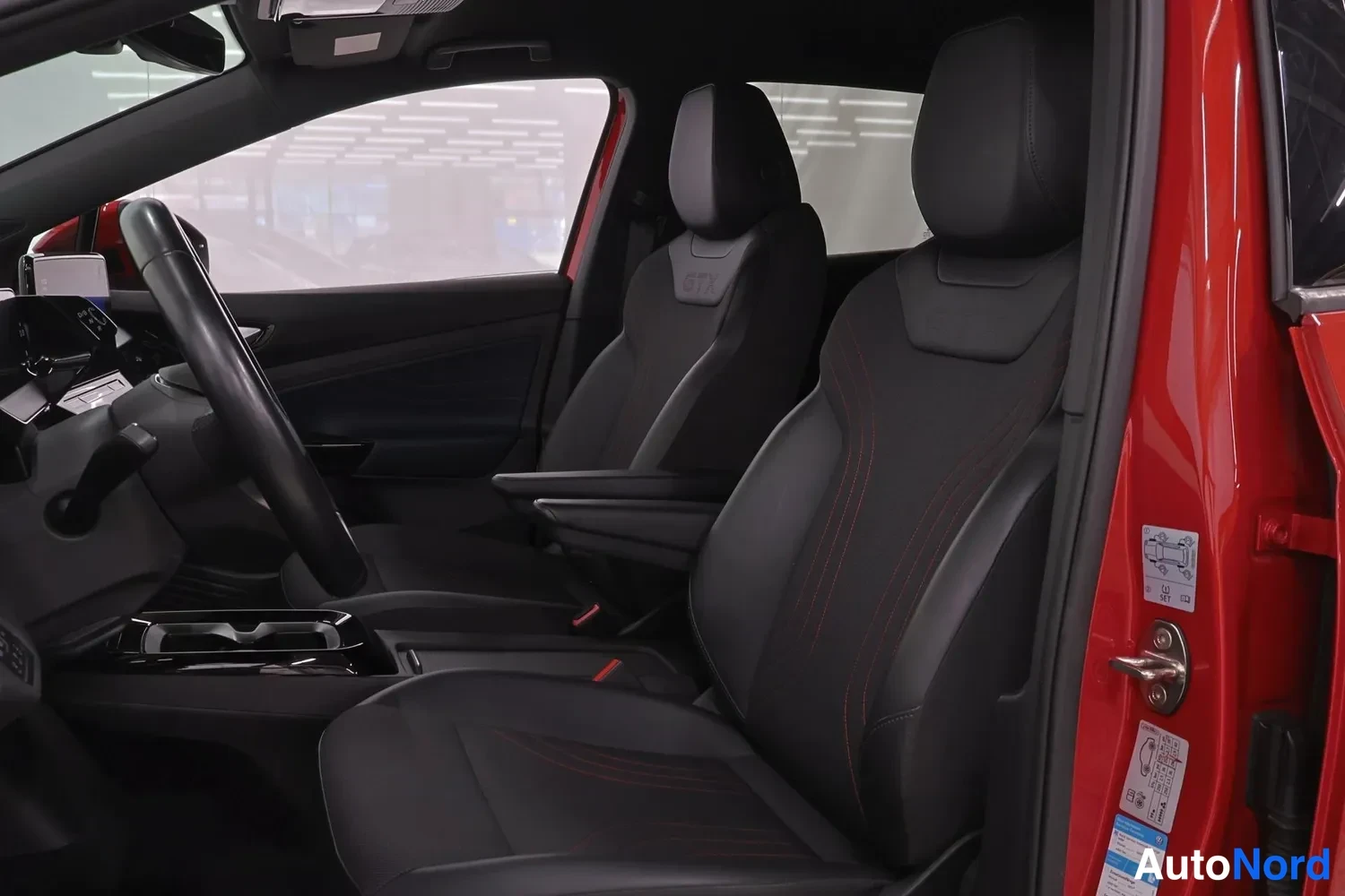 Muu: Volkswagen ID.4 GTX:n etummat istuimet, mustat istuimet punaisilla ompeluksilla ja GTX-logolla, ajoneuvon sivuovi auki rekisterikilpien lisätarroineen.
