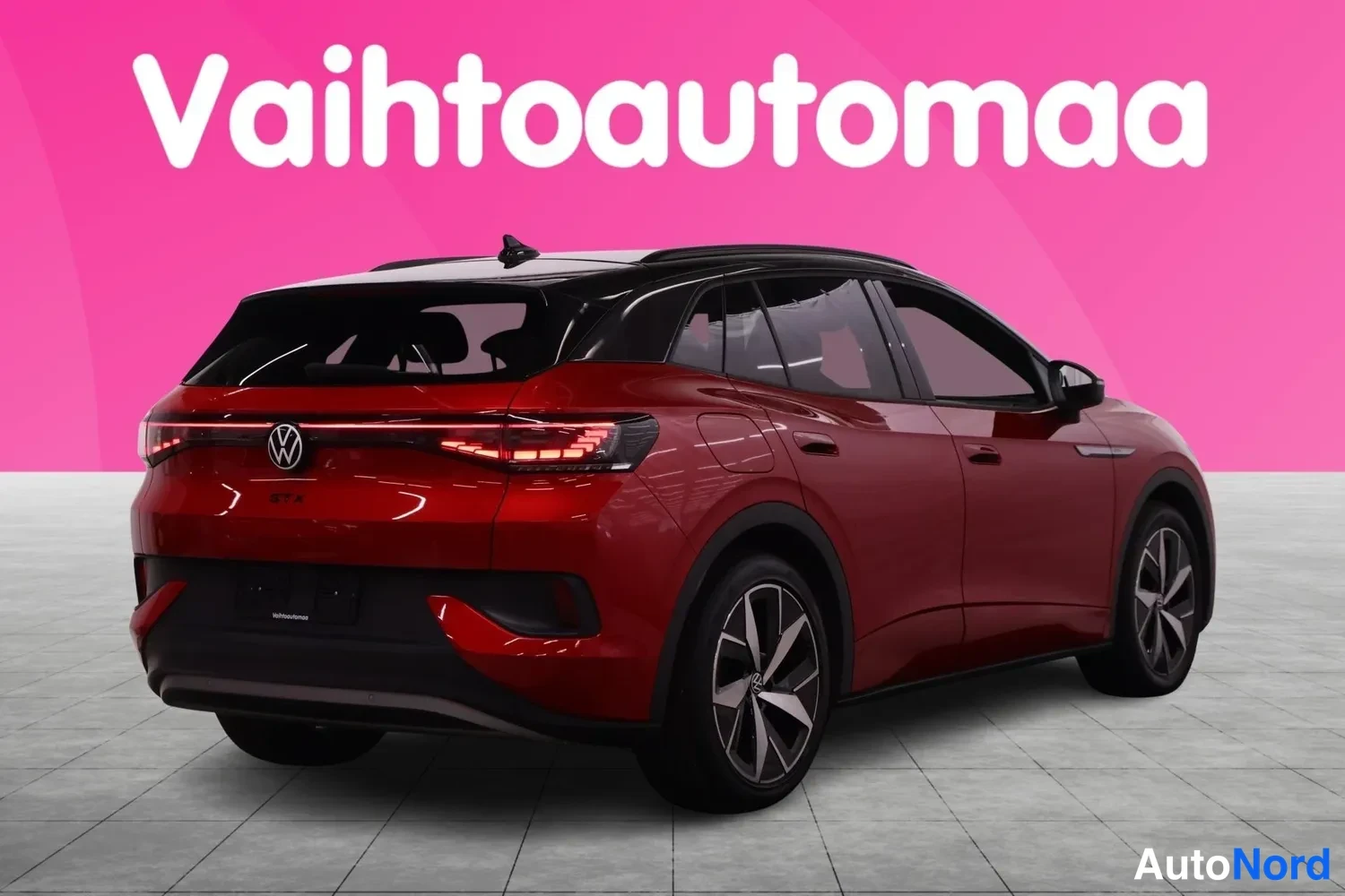 Takaviisto: Punainen Volkswagen ID.4 takaa kolmannenvälinen kulmakuva, musta katto ja vihreät LED-takavalot studiohouden, taustalla pinkki mainosseinä.