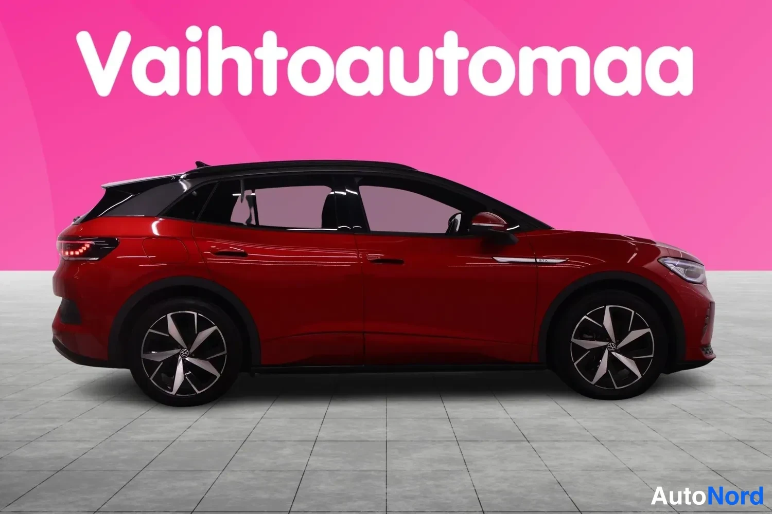 Etuviisto, nokka oikealle: Punainen Volkswagen ID.4 sivulta kolmannenvälinen kulmakuva, keula oikealla, harmaat seosvanteet ja musta viistokatto studiohoudessa.